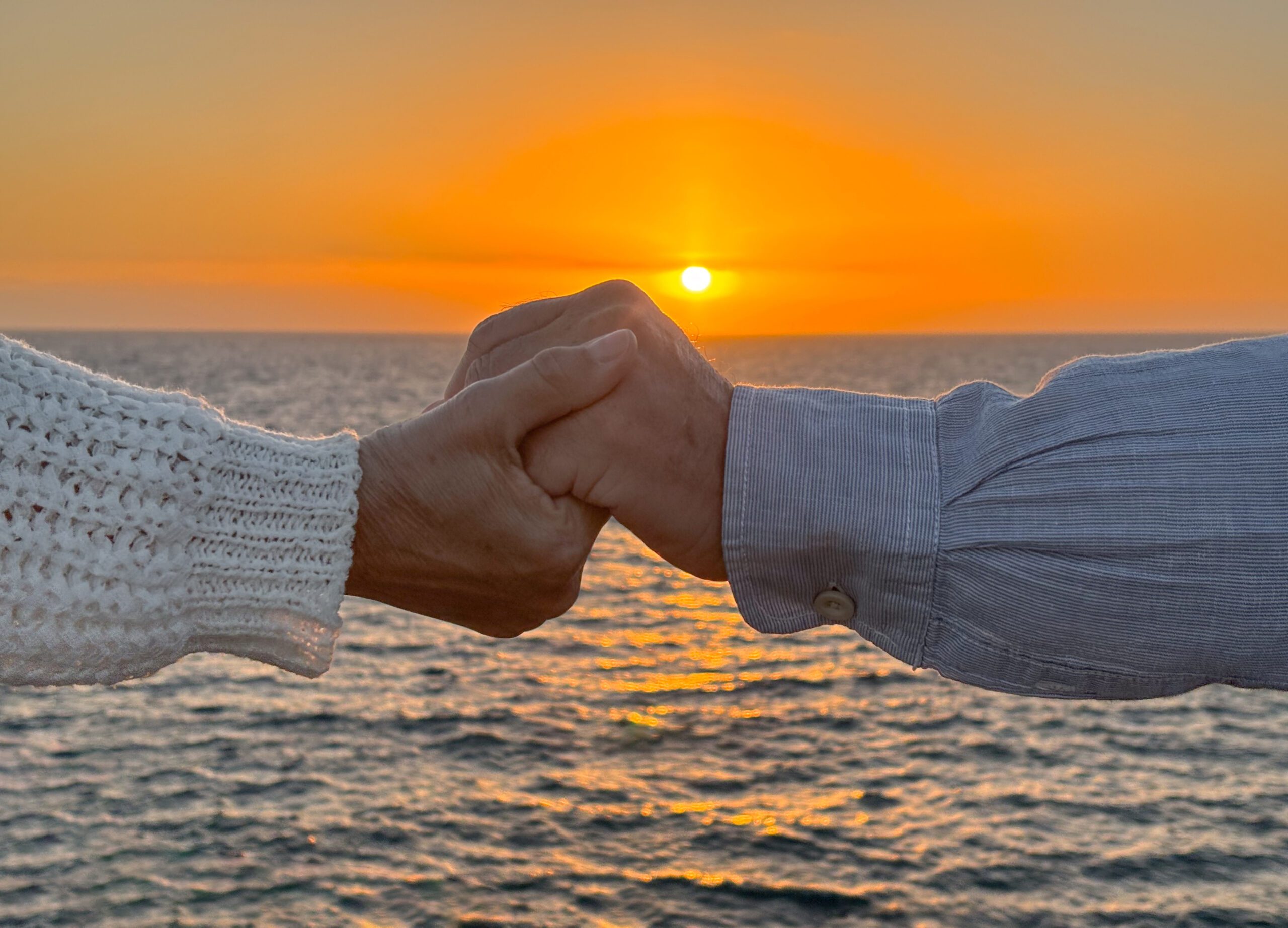Close-up of two mature hands holding each other at sunset by the