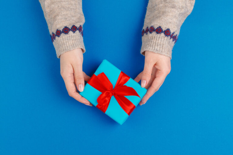 Small gift box in female hands on blue background, view from above